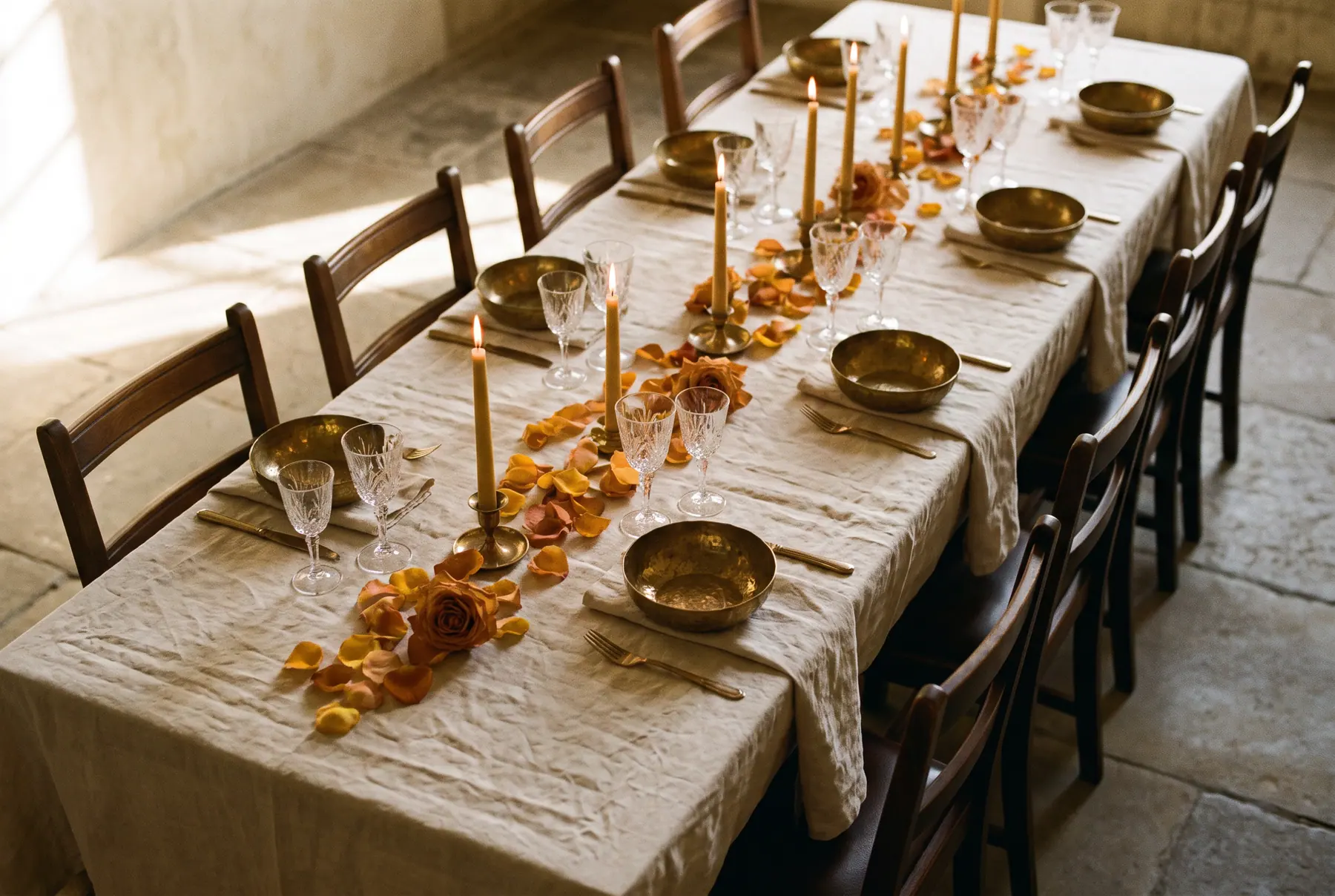 A long banquet table laid in bone linen and brass, lit by low candlelight.