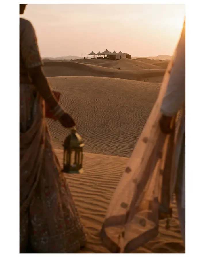 Desert dunes at sunset with a distant tented camp.