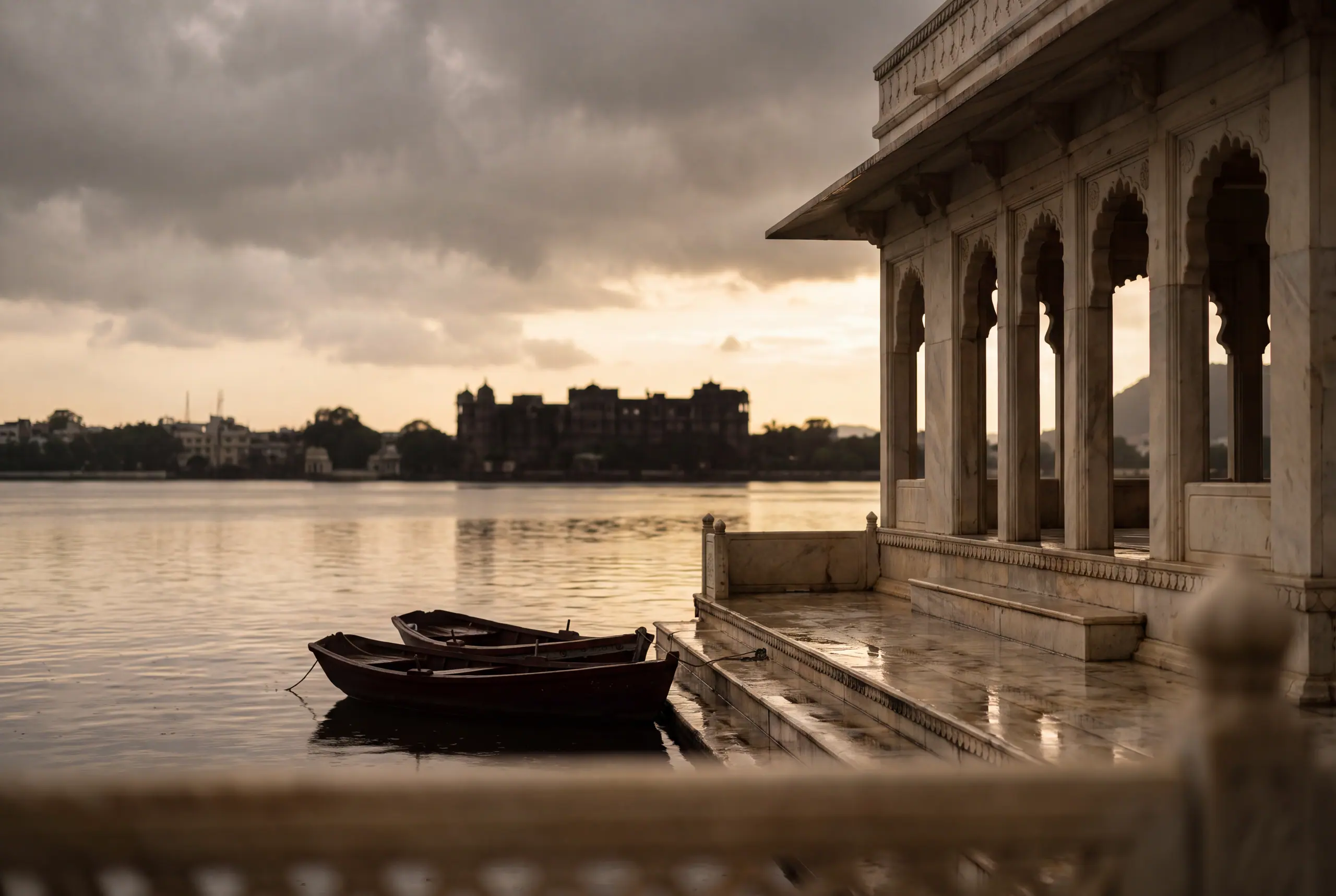 A lakeside marble pavilion in monsoon light, boats moored below.